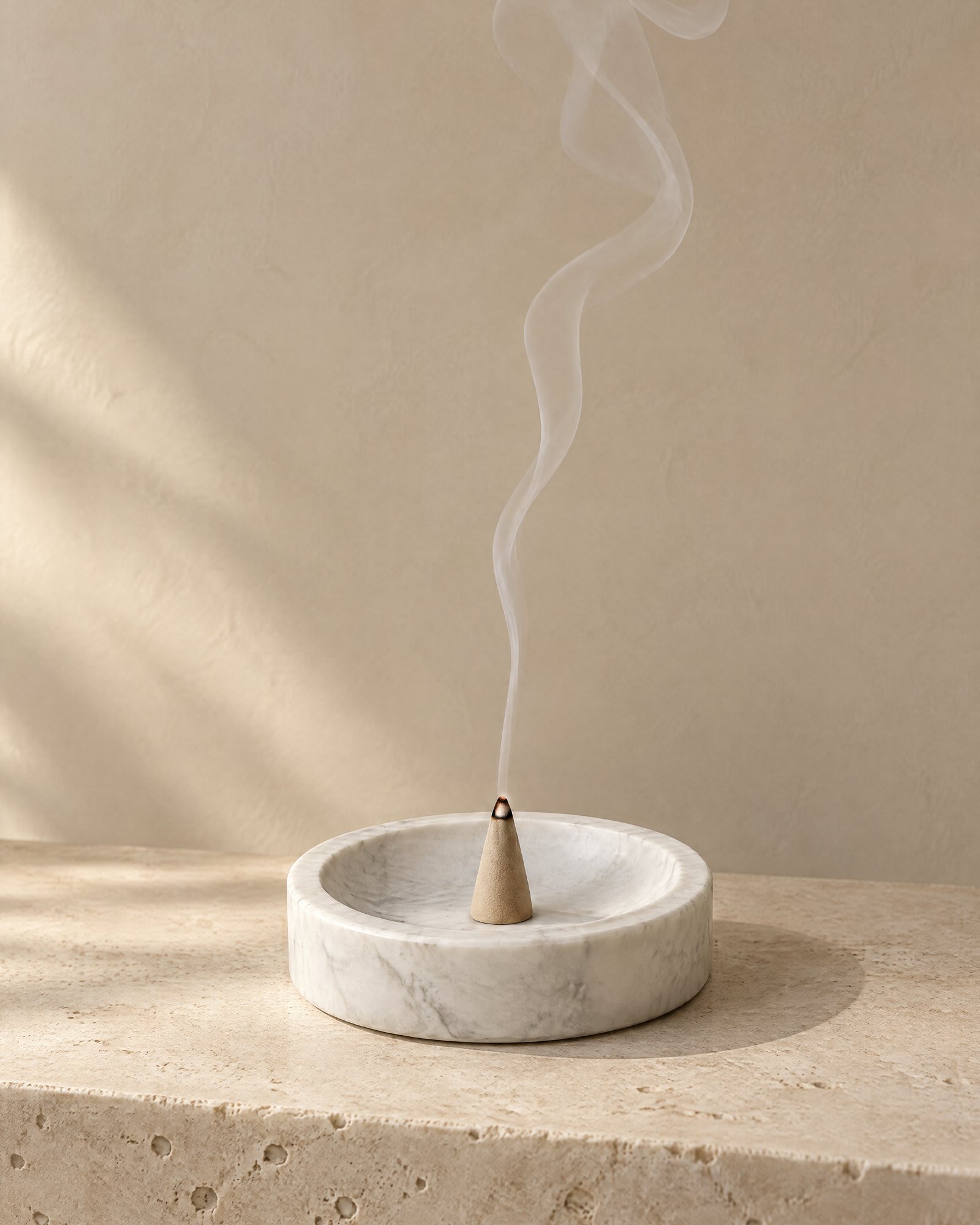 An incense cone burning on a marble dish, a ribbon of smoke against a plaster wall
